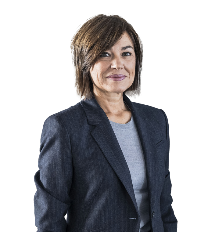 Eine Person mit dunklem, schulterlangem Haar trägt einen lila Blazer und ein weißes Oberteil, steht mit verschränkten Armen vor einem weißen Hintergrund.