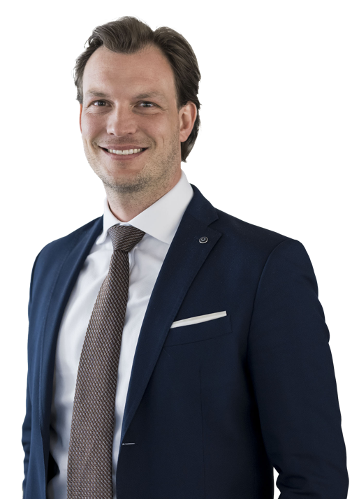 Ein Mann in einem dunklen Anzug mit weißem Hemd und Krawatte lächelt in die Kamera.