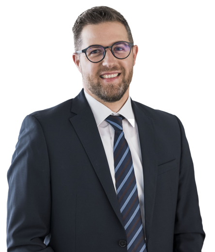 Eine lächelnde Person in einem Anzug und Hemd vor weißem Hintergrund.